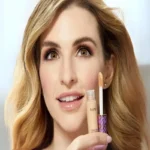 A woman displays a full-size tube of Tarte Shape Tape Contour Concealer, shade 22B Light Beige, in her hand.