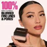 A woman displays HUDA BEAUTY Easy Bake Loose Powder labeled 100% with a focus on the Sugar Cookie shade.