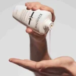 A person holding a bottle of Kérastase Specifique Bain Prevention Shampoo for thinning hair, 250ml, silicone-free.